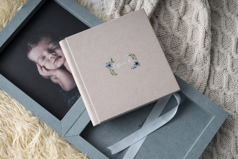 open photography album presentation box with a photo of a baby. small album resting on top of box.