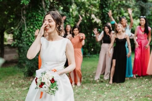 wedding photograph of smiling bride outside in garden about to throw her bouquet of flowers to her friends