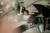 bride and groom sat at a grand piano on their wedding day