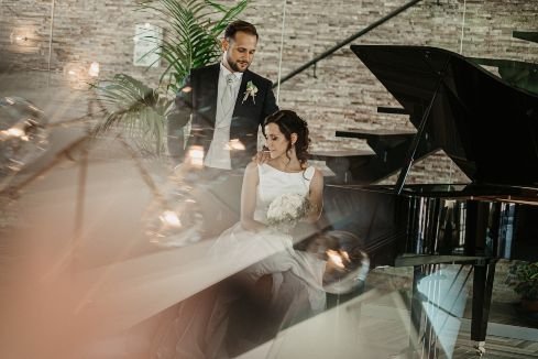 wedding photograph of bride and groom sat at a grand piano