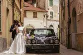 stylish modern couple on their wedding day celebrating with champagne and kissing next to a vintage car