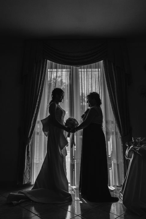 Black and white wedding photograph of bride holding hands with her mother before going to church