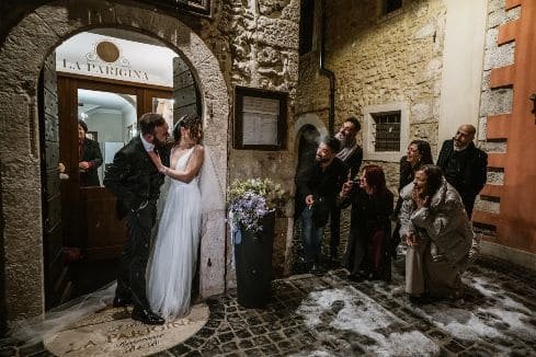 married couple on their wedding day kissing as their friends peak from around the corner.